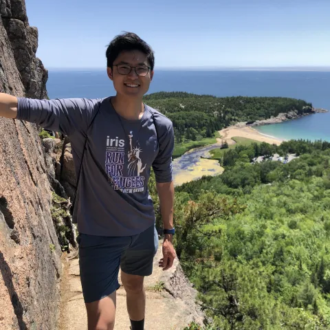 Kevin standing on the edge of a cliff overlooking the ocean and forest. 