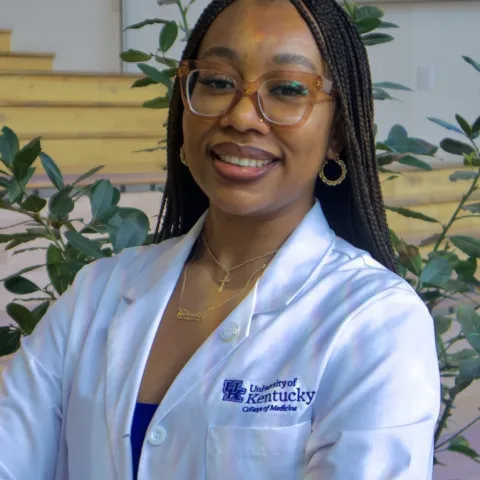 Student in her white coat in front of a plant
