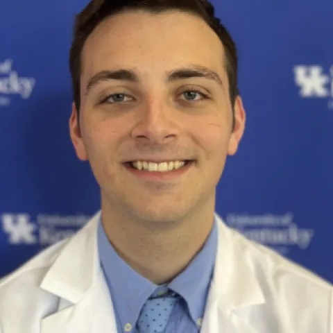 Student in white coat standing in front of UK background.