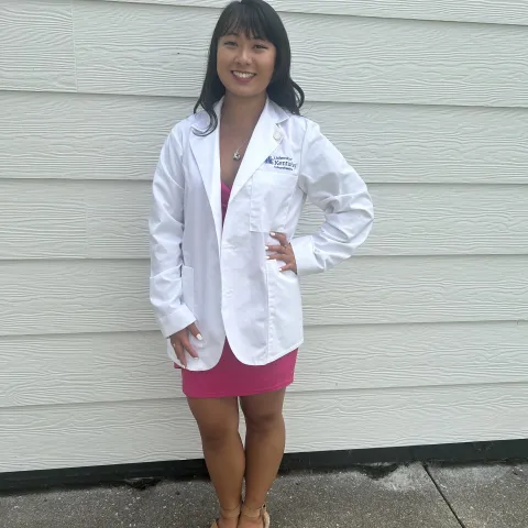 Student in white coat standing outside in front of a wall.