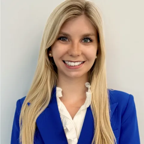 Student with blue blazer standing in front of a white wall.