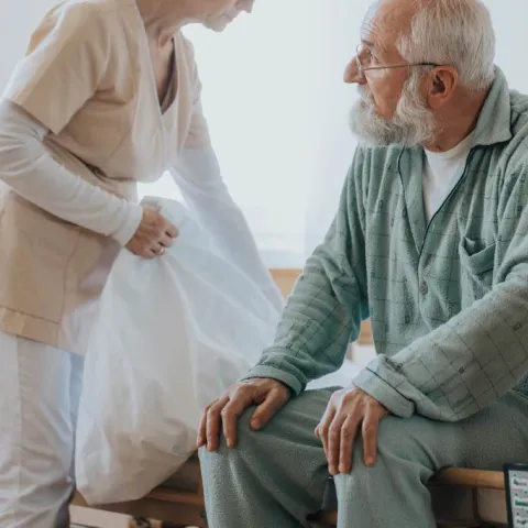 A nurse fluffing up an elderly patient's bedding. 