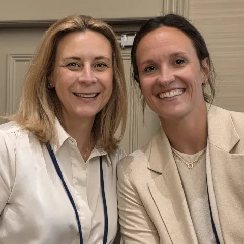 Two women in cream colored blouses smiling seated together