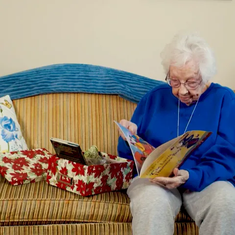 An elderly woman sitting on a couch, exploring a memory box. 
