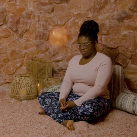 A woman is meditating within a salt cave to practice self care. 