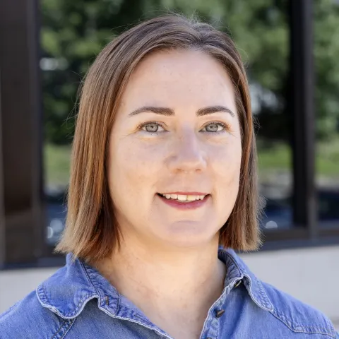 Kelly Parsons wears a denim button-up while smiling for a photo. 