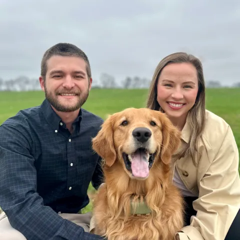 Kathryn Fox and another individual flank a golden retriever, who appears to be their pet