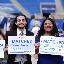 Two smiling students at Kroger Field hold signs reading "I MATCHED!" with details of their medical residency matches.