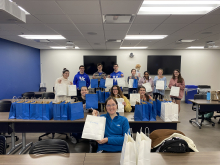 various students hold up blue and white gift bags from a care package packing event