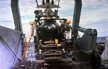 A submersible sits on a ship's deck under a large crane arm. Its spherical, metallic body is surrounded by equipment. | Photo provided by Dr. Gerhardt