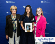 Two women flanking a young woman in a black dress holding a picture frame, smiling