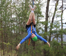 Ward, wearing a helmet and harness, hangs upside down from a zipline in a wooded area, stretching her arms wide and smiling. Outside of medical school, Ward enjoys spending time outdoors.