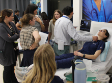 Dozens of endocrine surgery fellows observe as a trainer coaches one of them in an ultrasound simulation of a medical student volunteer's neck.