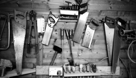 lots of tool hanging on a wooden wall:  saws, bolt cutters, wedges, hammers, etc.
