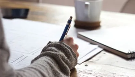 hand holding a pen and writing on a piece of paper