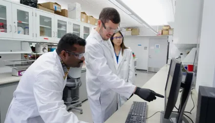 A photo of Dr. Brad Hubbard with members of his lab looking at a computer screen 