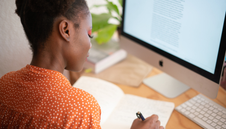 A woman in an orange shirt working at a computer desk.