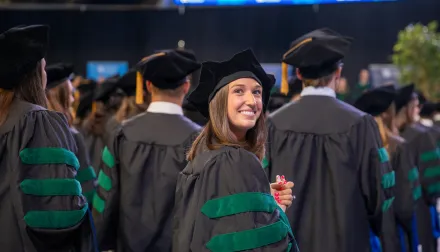 graduation ceremony for the glass of 2025. students standing in cap and gown with a female graduate looking back 