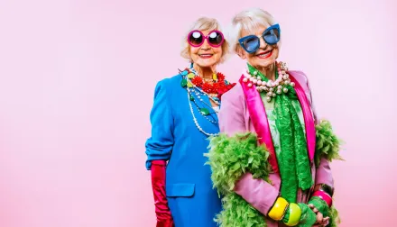 Elderly women are dressed up in colorful clothes against a pale pink background. 