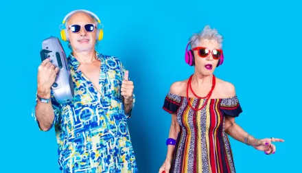 Elderly couple is dressed up in silly, colorful disco clothes against a blue background. 