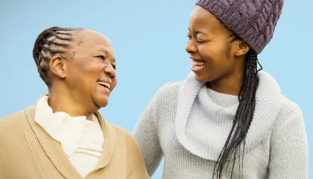 An elderly woman is smiling at her adult daughter against a blue background. 
