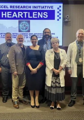 The EXCEL group stands together in front of a screen that says "Excel Grant Initiative - HeartLens"