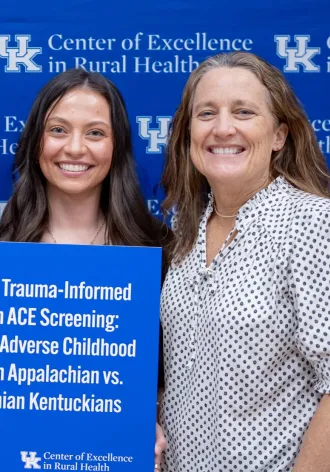 3 people pose in front of a blue background holding a poster that says "Implementing Trauma Informed Care through ACE Screening: Understanding Adverse Childhood Experiences in Appalachia vs Non-Appalachian Kentuckians