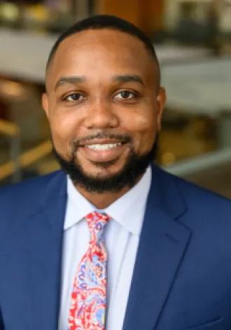 Headshot of Justin Xavier Moore in a blue suit