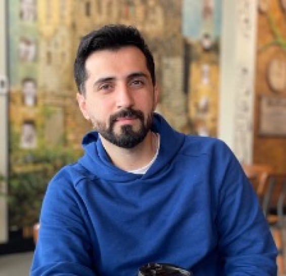 Dr. Feizy smiling at camera with a blue sweater and a coffeeshop in the background