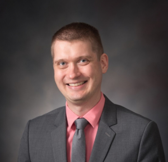 Dr. Koffarnus in a grey suit, salmon shirt, and grey tie smiling at the camera.