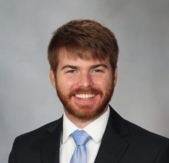 photograph of a man with short hair and beard in a suit with a blue tie