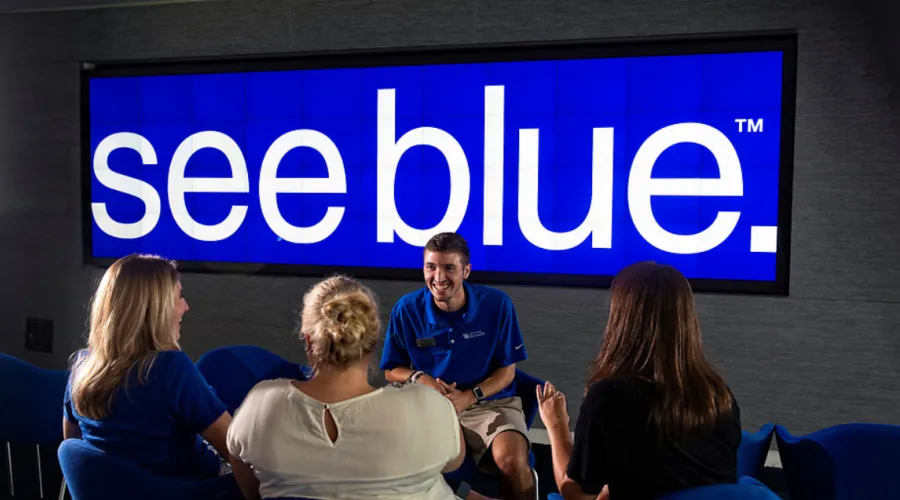 Visitors with touring guide in front of a sign that reads, "See Blue."