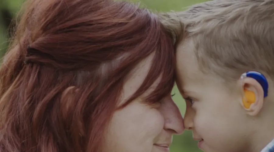 Mother and child with hearing aid pressing their foreheads together.