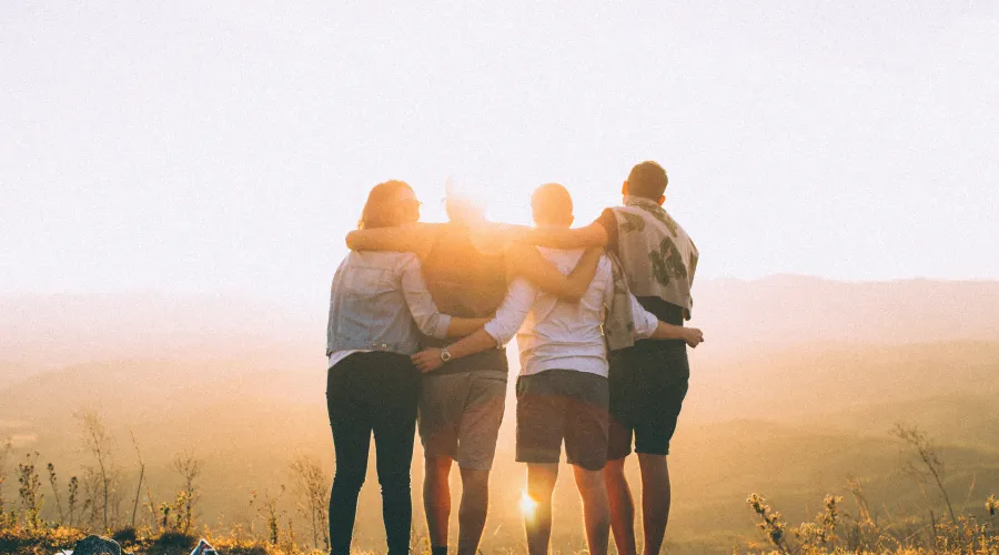 4 individuals arms entwined standing side-by-side with a sunset in background