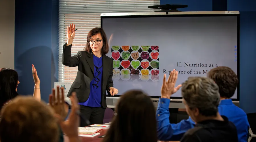 speaker and crowd raising their hands; screen in background with pictures of food