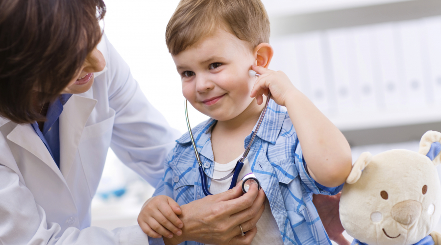 provider standing next to child with stethoscope; stuffed bear to the side
