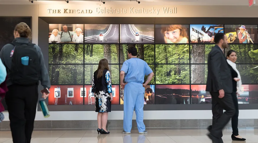 two people standing in front of the large display screen in the hallway of Chandler Medical Center