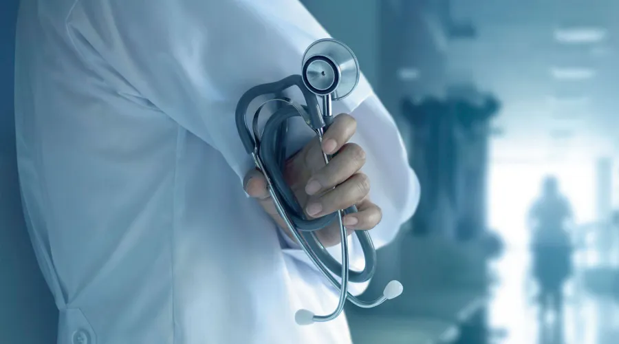 person holding stethoscope standing in a hospital hallway