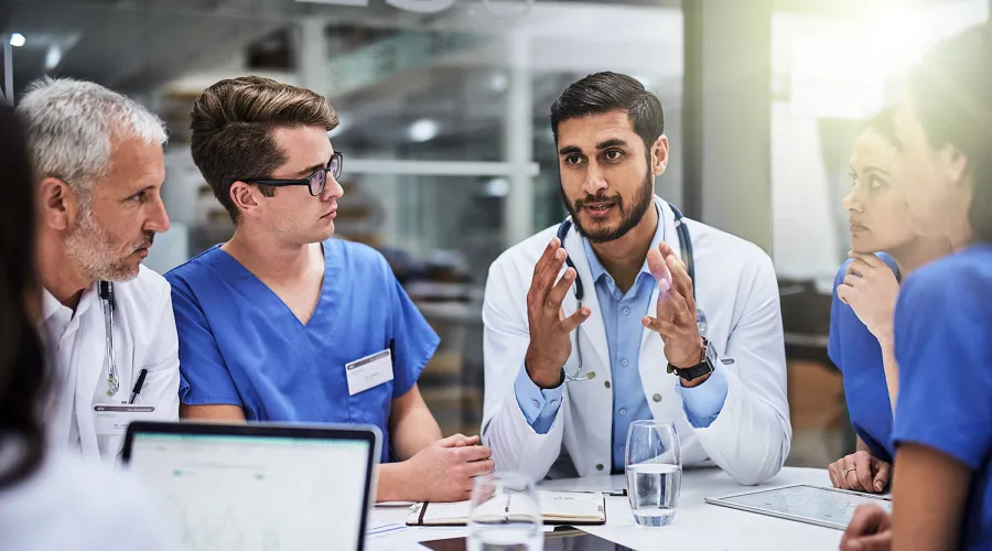 group of medical professionals sitting at a table discussing; water glasses and computers also on table