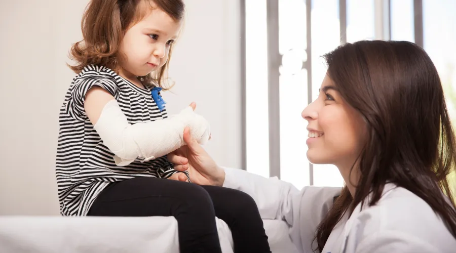 provider squatting next to child on exam table with arm wrapped