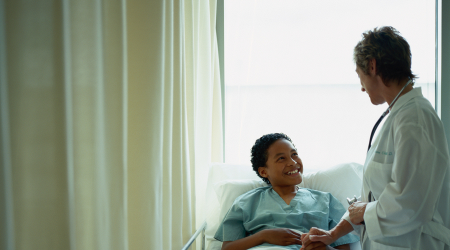 child in hospital bed with provider standing at side of bed