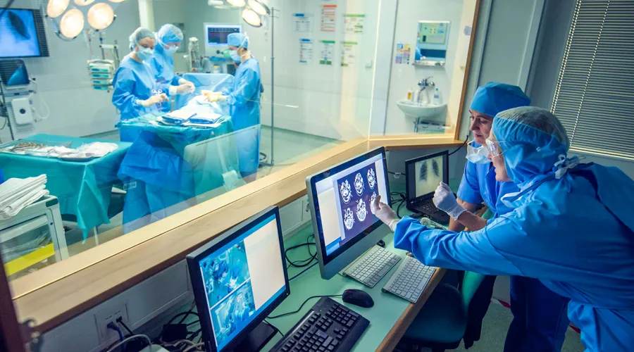 2 providers looking at a screen while surgery is being completed on the other side of a glass divide