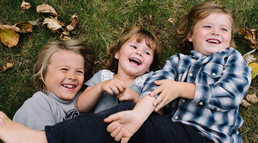 three kids laying on the grass and laughing