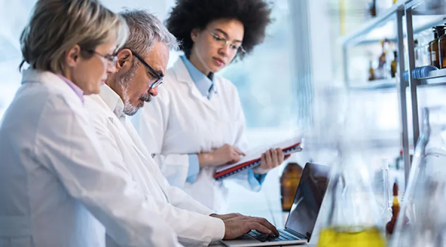 3 researchers standing in laboratory looking at some result