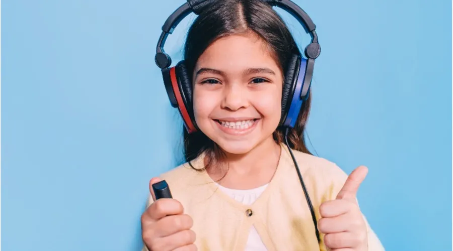 A smiling child doing a hearing test with earphones and a thumbs up.