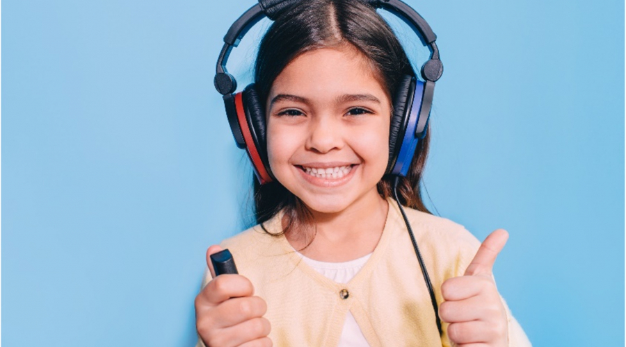 A smiling child doing a hearing test with earphones and a thumbs up.