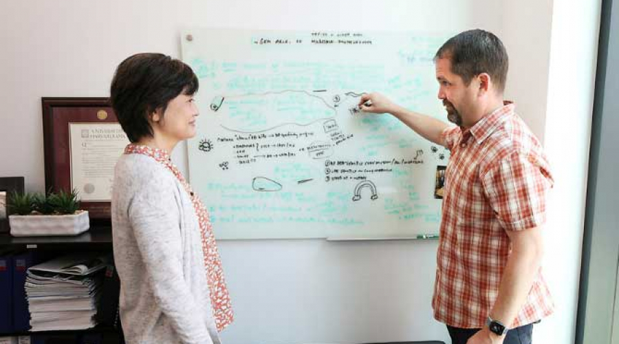 researchers Fardo and Katsumata looking at information on a white board