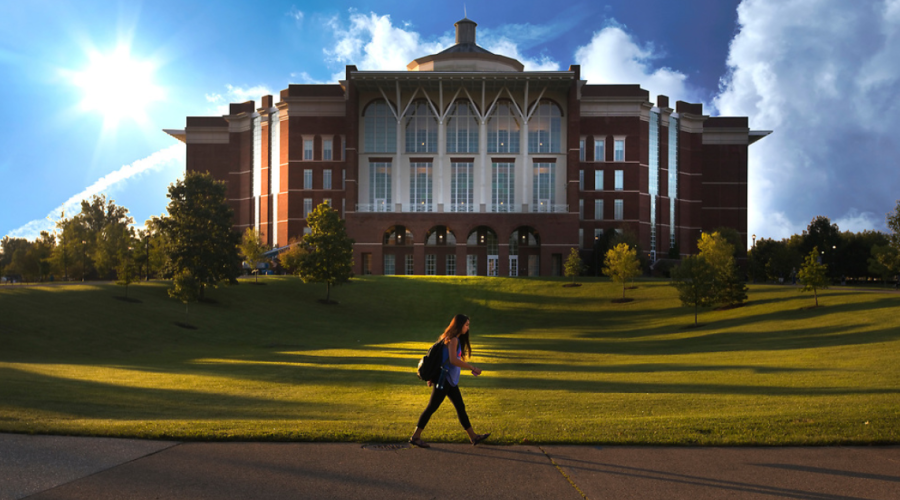 Student walking in the green field in front of the library.