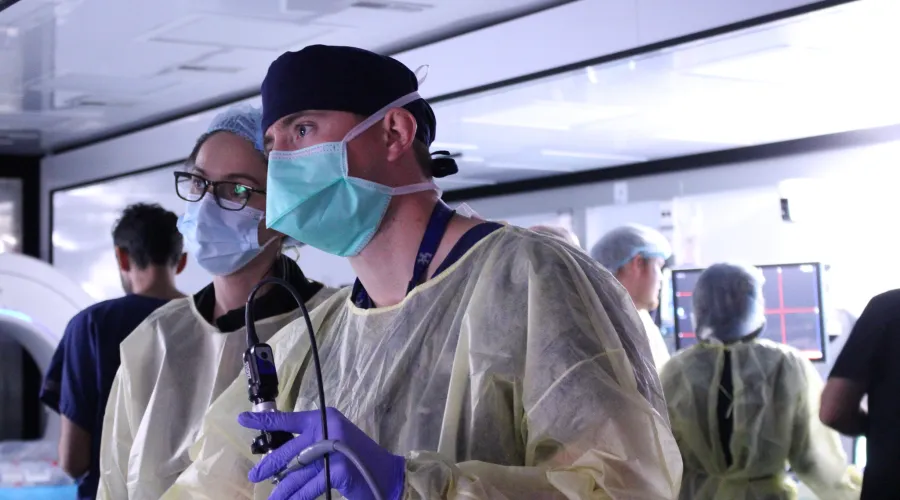 Two residents caped and scrubbed, holding a scope on a figure off screen.