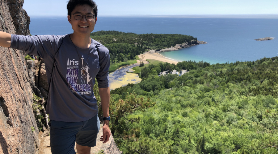 Kevin standing on the edge of a cliff overlooking the ocean and forest. 